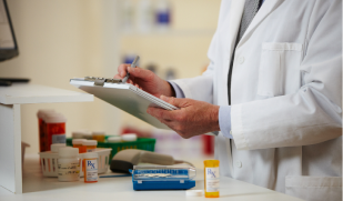 Pharmacist in a white coat writing on a clipboard near prescription bottles and a pill counter.