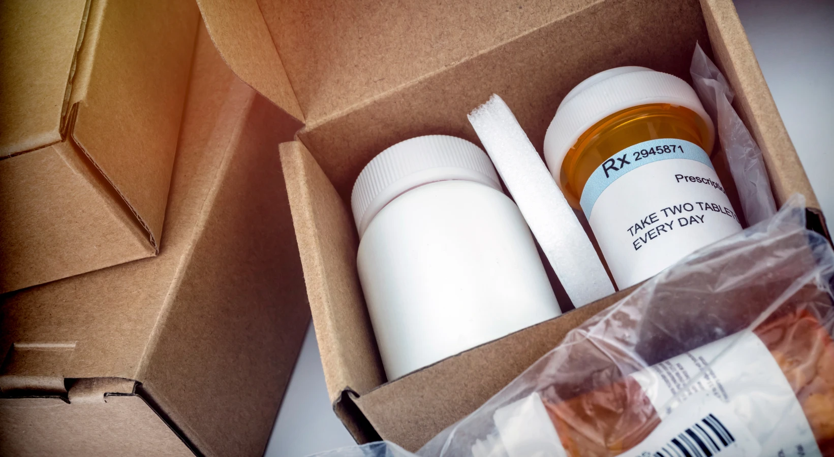 Two prescription pill bottles packed in a cardboard shipping box, one with a visible pharmacy label.