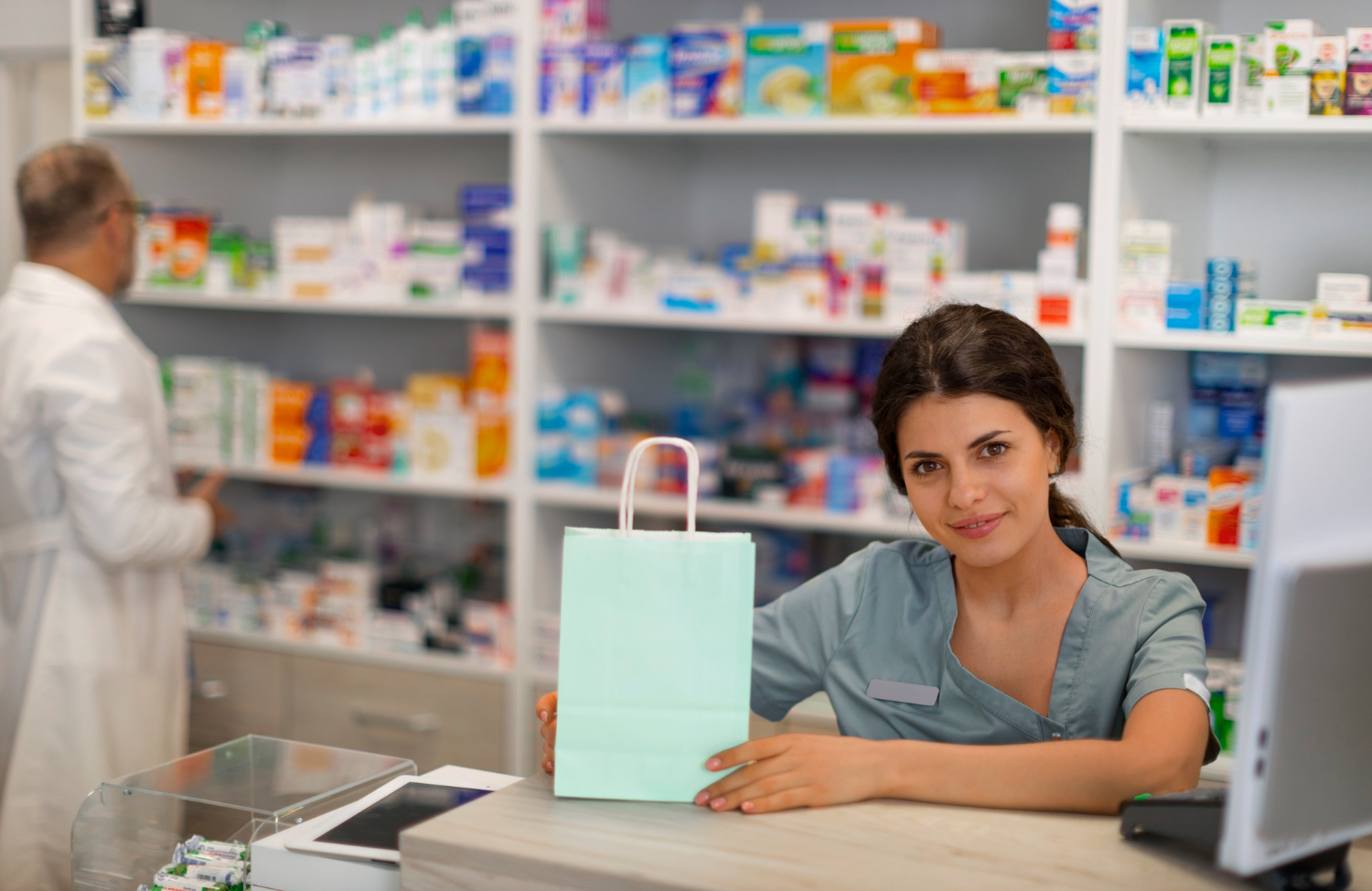 2150600102 Pharmacist hands a paper bag to a customer at the counter with medicine shelves in the background.
