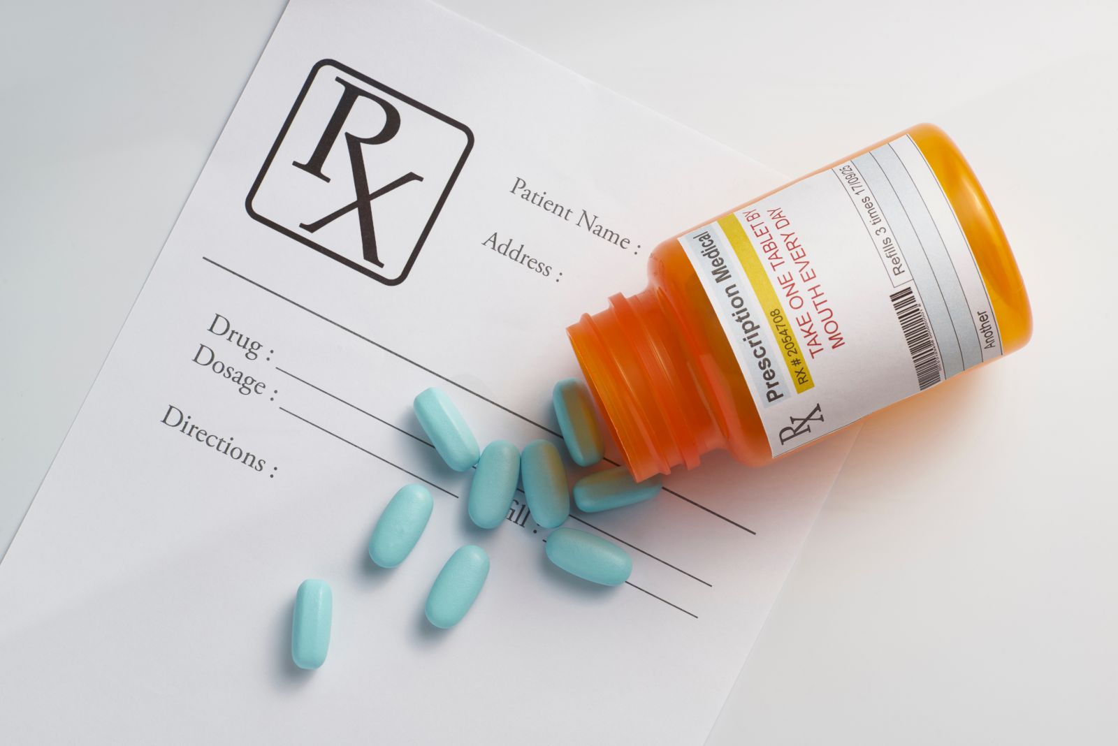 AdobeStock_117966107 Orange pill bottle with blue pills spilled on a prescription form with empty fields for patient and drug details.