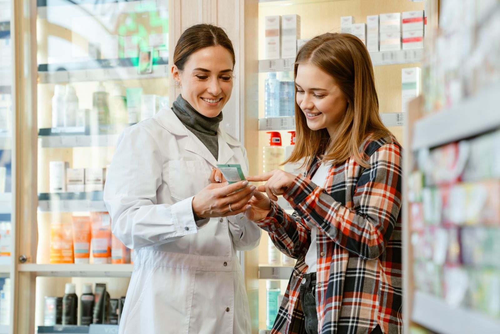 A pharmacist helps a smiling customer choose a product in a pharmacy aisle.