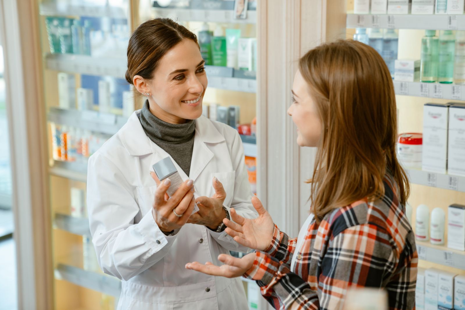 A pharmacist shows a product to a smiling customer in a pharmacy aisle.
