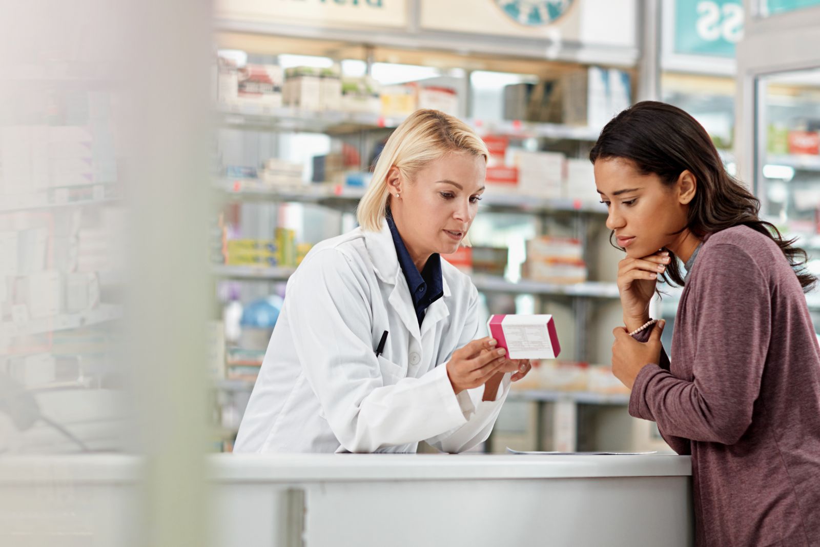 A pharmacist explains medication instructions to a concerned woman at a pharmacy counter.