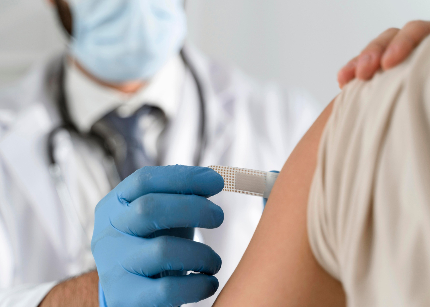 A doctor in gloves gives a vaccine injection to a patient's upper arm.