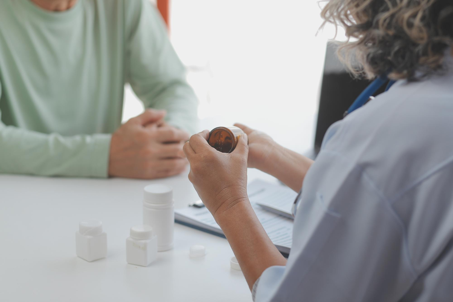 Doctor showing a pill bottle to a patient during a consultation at a desk with medicine containers.