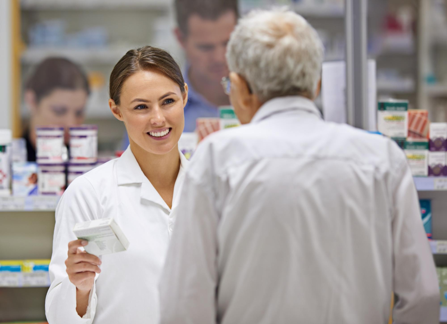 A pharmacist smiling and handing medication to a customer in a pharmacy.