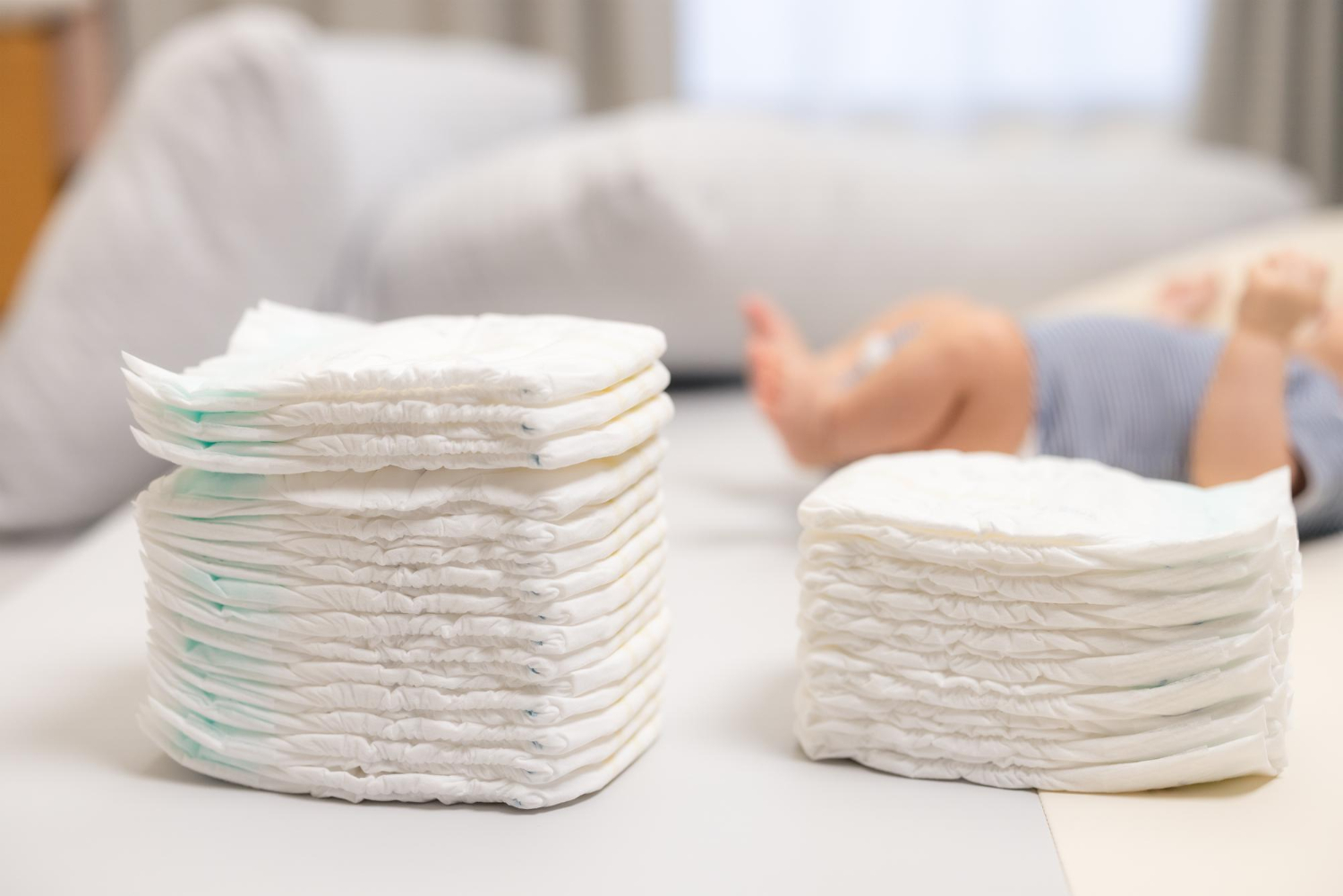 32255 Two stacks of diapers on a table with a baby lying in the background, slightly out of focus.