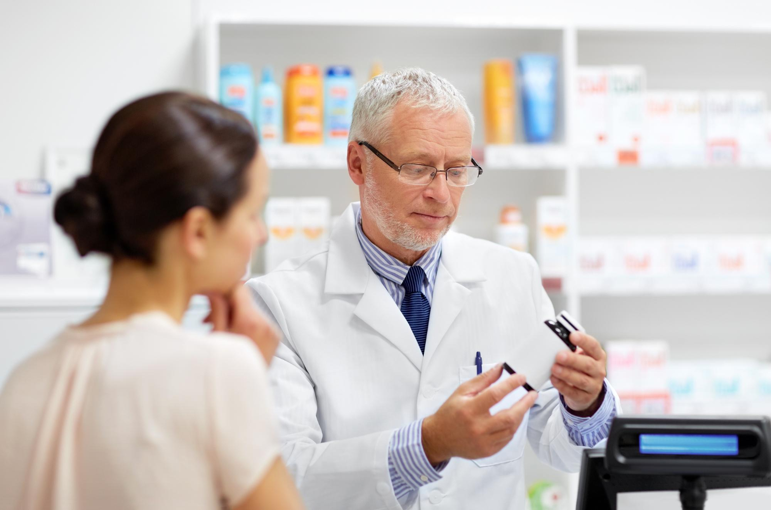 213178 Pharmacist showing medication to a woman at the counter in a pharmacy, with shelves of products behind them.
