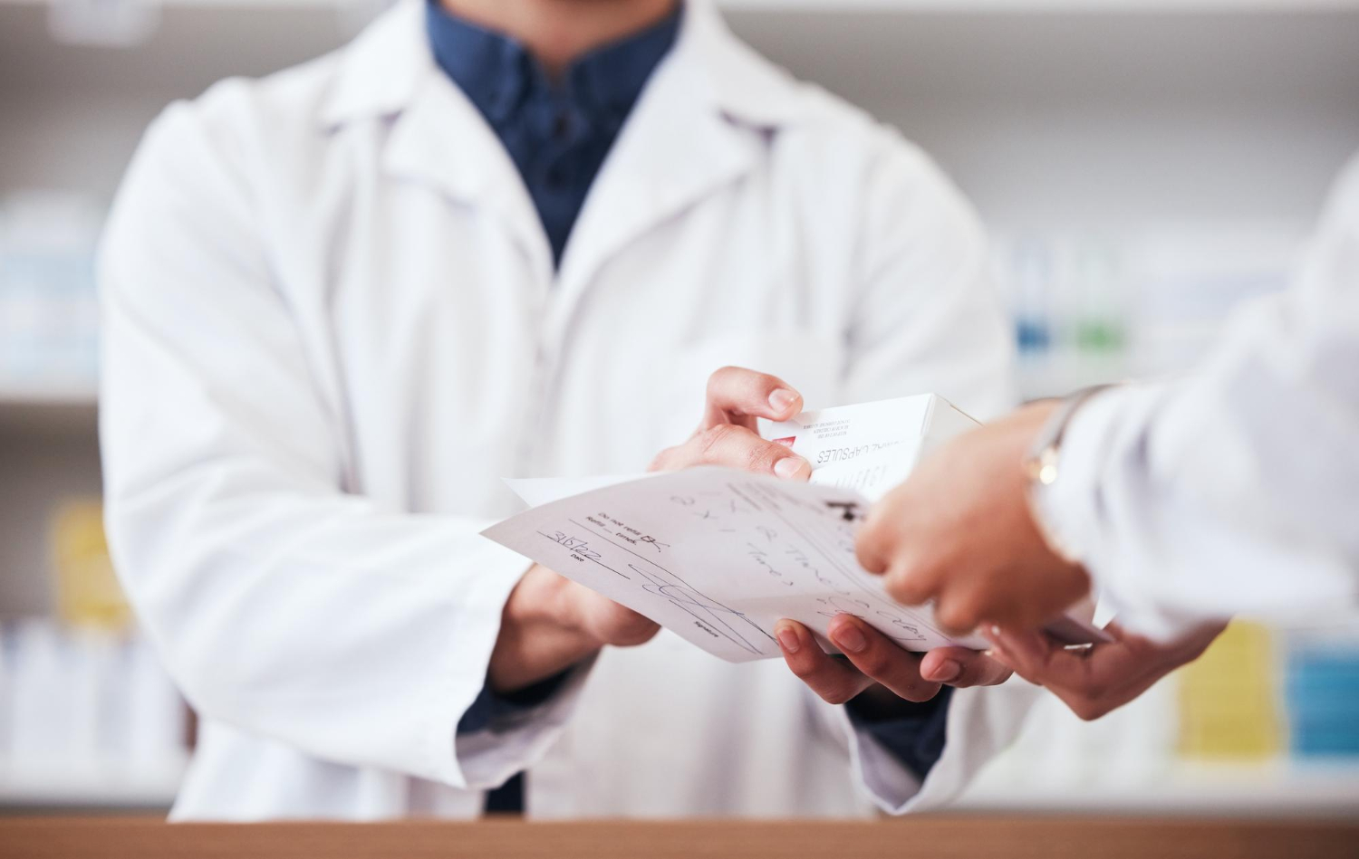 221557 A pharmacist hands a prescription and medication to a customer across a counter.